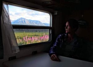 Woman looking out an RV window at Alaskan mountains